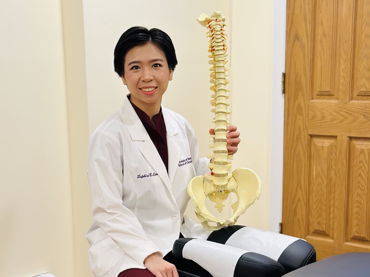 Dr. Sophia Lam, D.C. holding an anatomical spine and pelvis model at her Bayside chiropractic office
