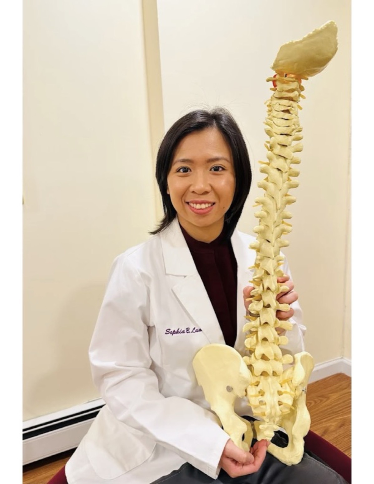 Dr. Sophia Lam, D.C. holding a full spine model in her Bayside, NY chiropractic clinic