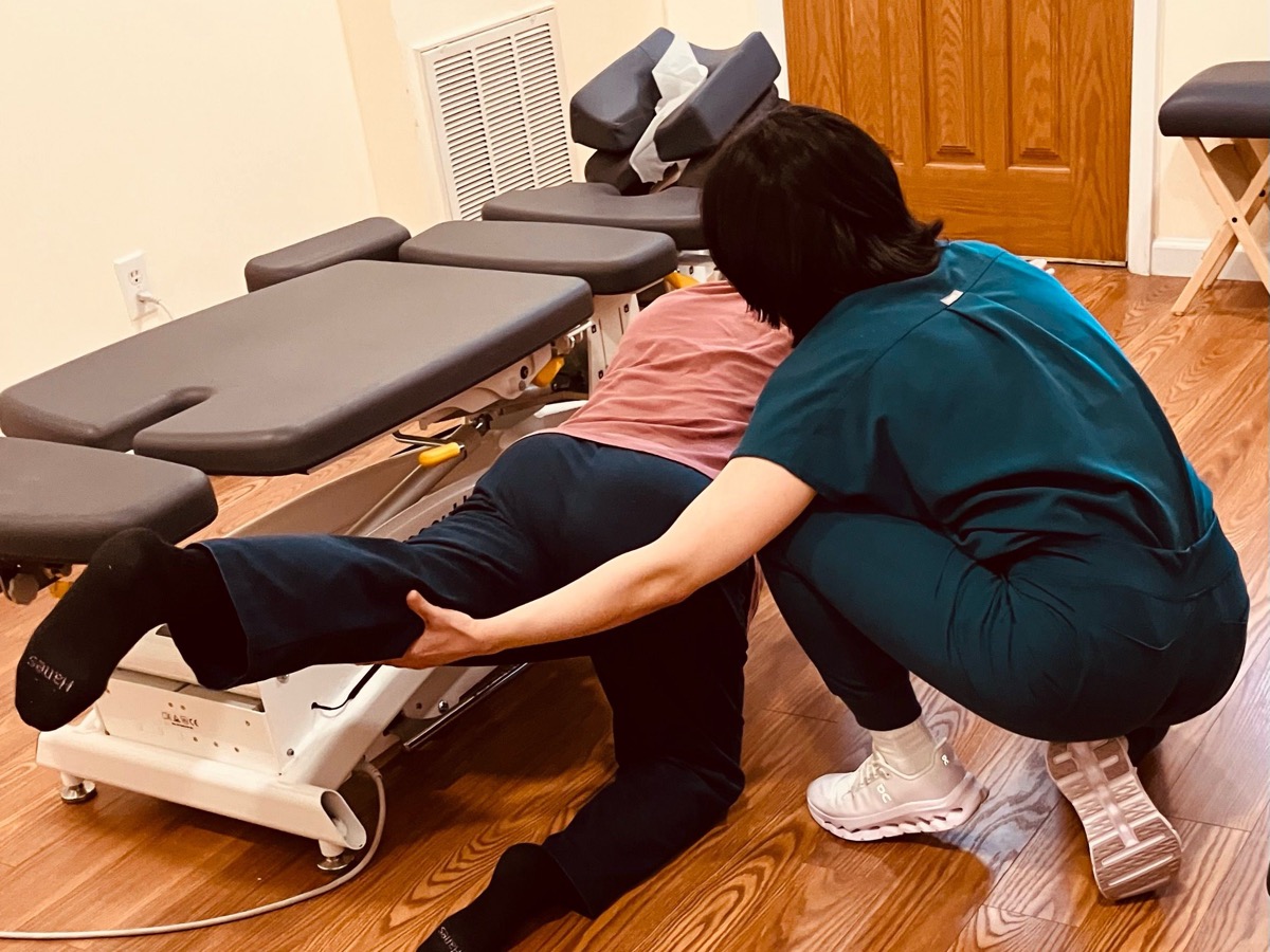 Dr. Sophia Lam guiding a patient through a leg and hip assessment on a treatment table at the Bayside clinic